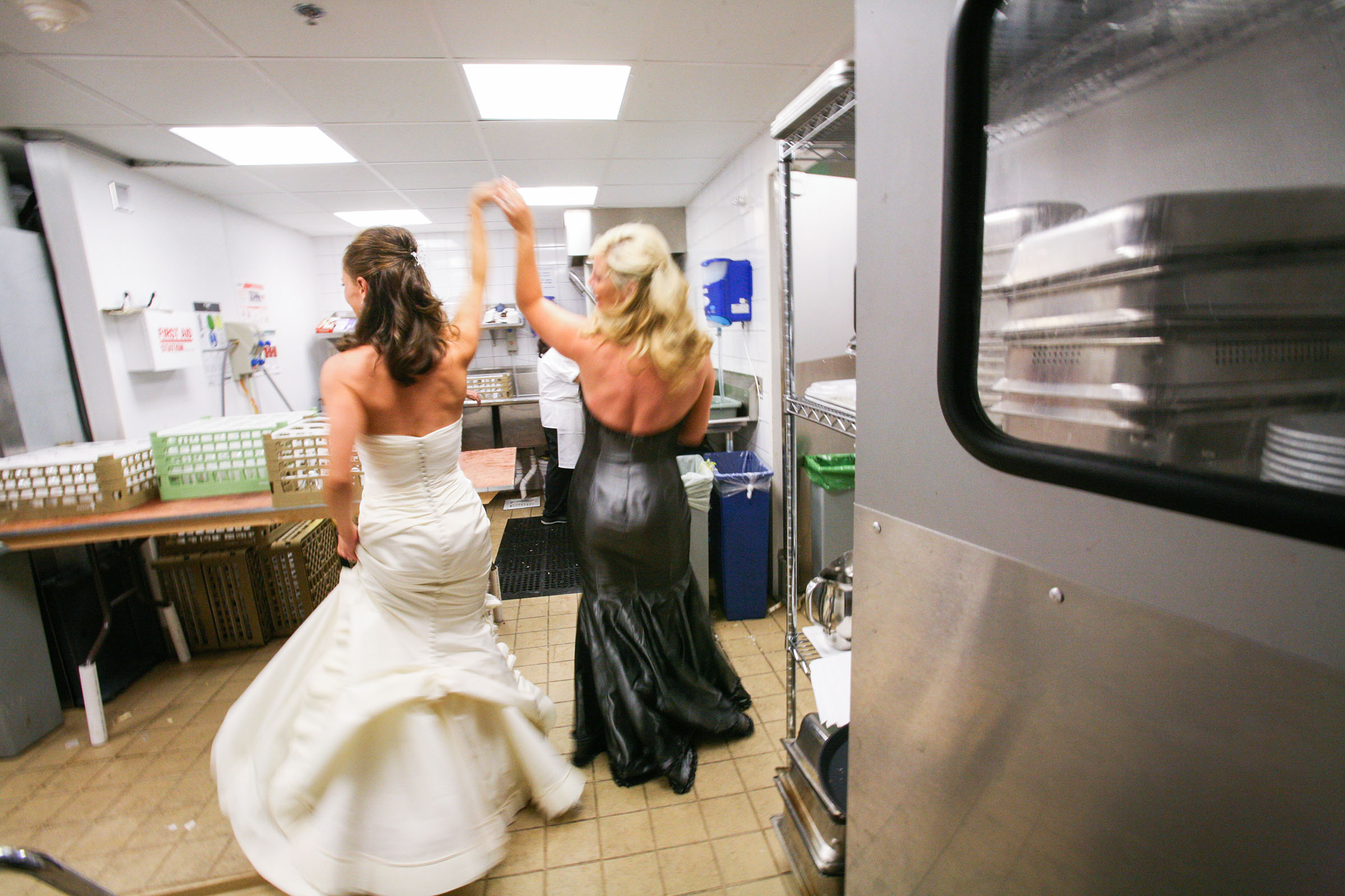 Bride and her bridesmaid dances into the kitchen at her wedding reception.